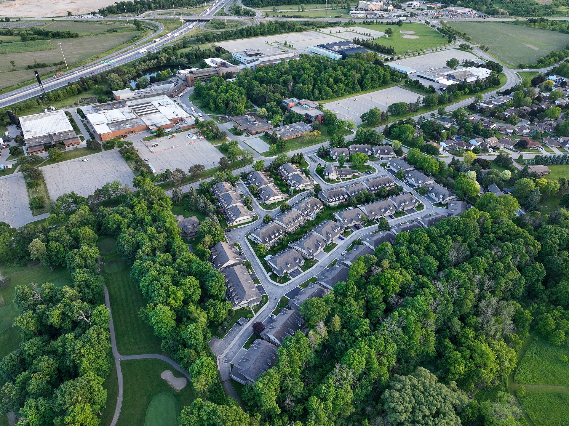 Aerial view of a residential development bordering a commercial park, with the arterial road and river valley behind