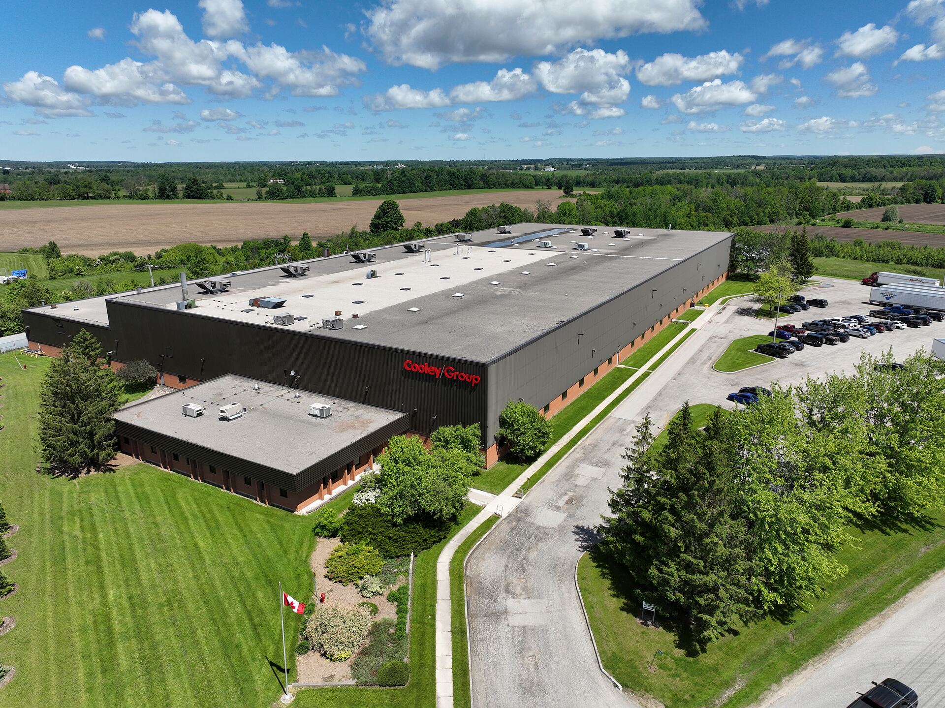 Aerial view of a manufacturing plant, its office wing, yard and access road, with farmland to the horizon