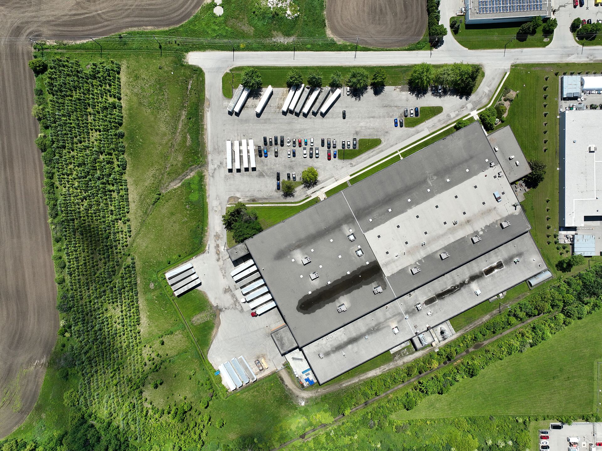Near-vertical aerial view of an industrial plant roof and its trailer yard, bordered by farmland, in southwestern Ontario